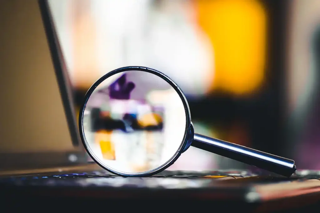 Magnifying glass resting on a laptop representing the evaluation and selection of a reliable CAT engine rebuild partner.